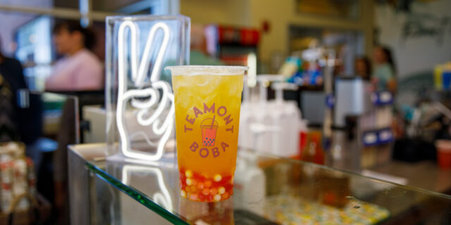 A boba tea with pink and white boba pearls in the bottom of the cup with a neon white peace sign behind it